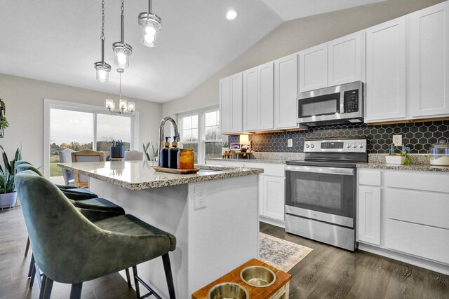 kitchen with stainless steel appliances, white cabinetry, a center island with sink, decorative light fixtures, and vaulted ceiling