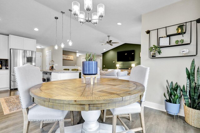 dining space with sink, lofted ceiling, wood-type flooring, and ceiling fan with notable chandelier