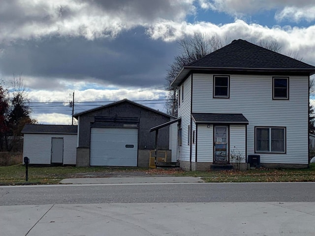 view of front of property with a garage, cooling unit, and an outbuilding