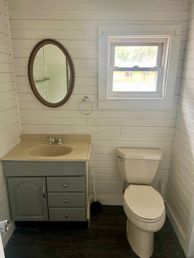 bathroom featuring vanity, hardwood / wood-style flooring, toilet, and wood walls