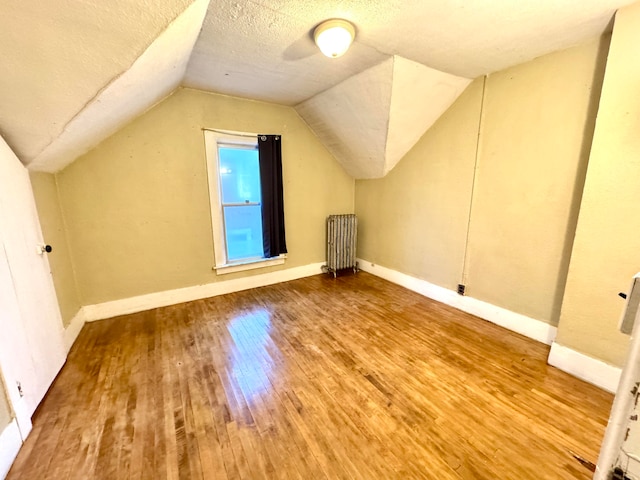 bonus room featuring radiator, a textured ceiling, wood-type flooring, and vaulted ceiling