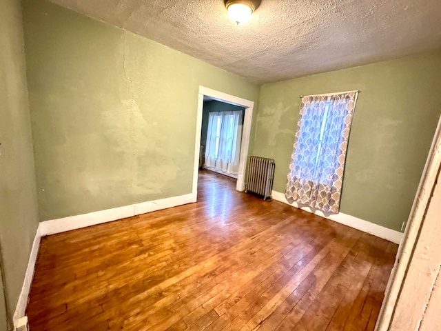 empty room with radiator heating unit, hardwood / wood-style flooring, and a textured ceiling