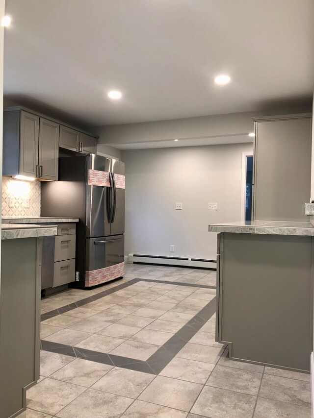 kitchen with decorative backsplash, baseboard heating, kitchen peninsula, gray cabinets, and stainless steel refrigerator