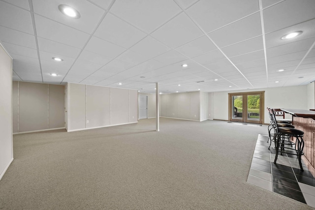 basement featuring bar area, a drop ceiling, french doors, and carpet floors