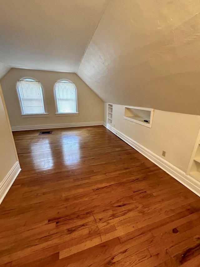 additional living space featuring built in features, hardwood / wood-style flooring, and vaulted ceiling