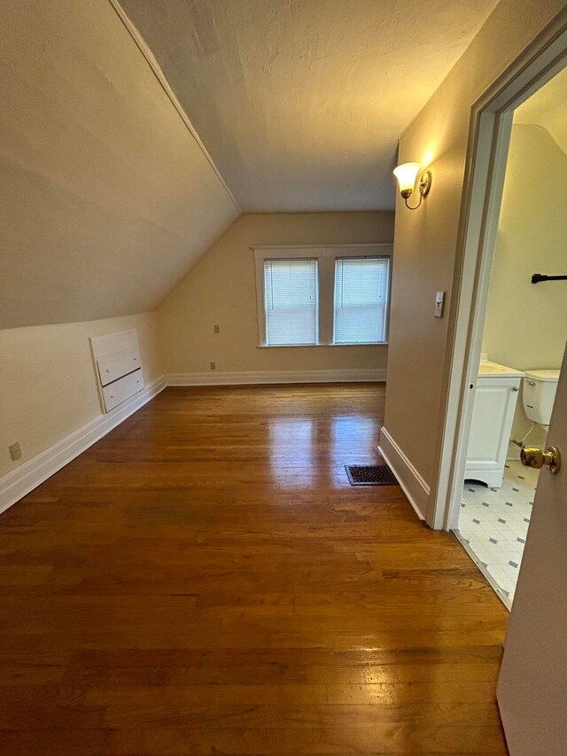 additional living space featuring wood-type flooring, vaulted ceiling, and a textured ceiling