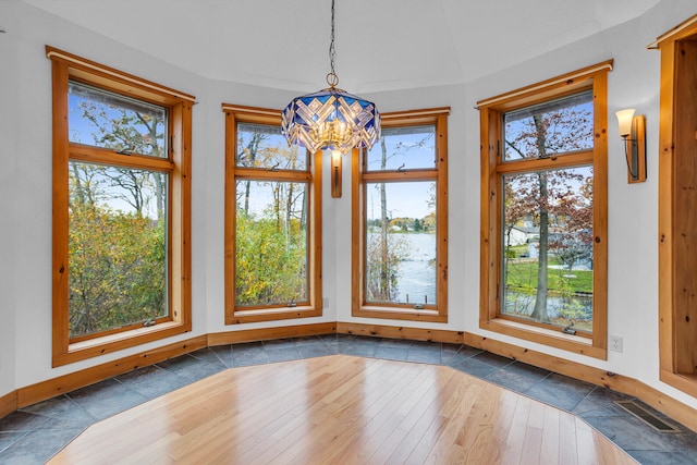 unfurnished dining area with a water view, an inviting chandelier, and dark hardwood / wood-style flooring