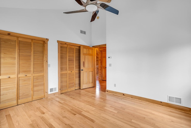 unfurnished bedroom with two closets, ceiling fan, light hardwood / wood-style flooring, and high vaulted ceiling