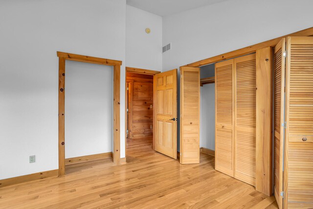 unfurnished bedroom featuring a towering ceiling, light hardwood / wood-style floors, and a closet