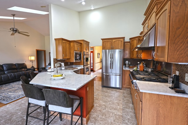 kitchen featuring sink, kitchen peninsula, appliances with stainless steel finishes, a breakfast bar area, and exhaust hood