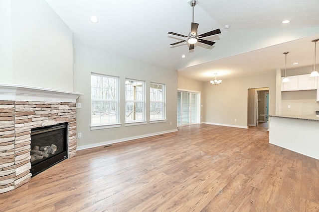 unfurnished living room with a stone fireplace, light wood-type flooring, high vaulted ceiling, and ceiling fan with notable chandelier