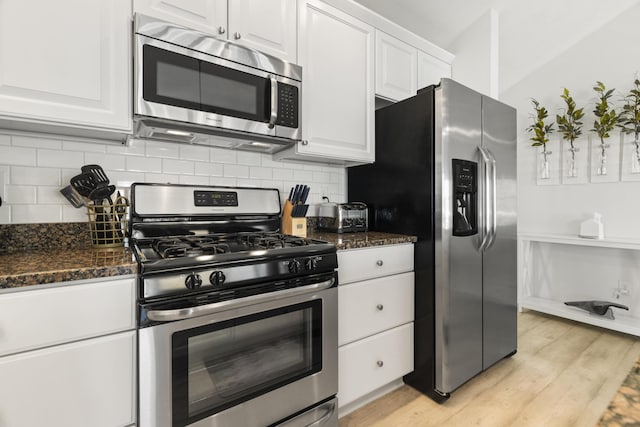 87 S Center St, Beulah, MI 49617 - kitchen featuring appliances with stainless steel finishes, white cabinets, light wood finished floors, tasteful backsplash, and dark stone counters