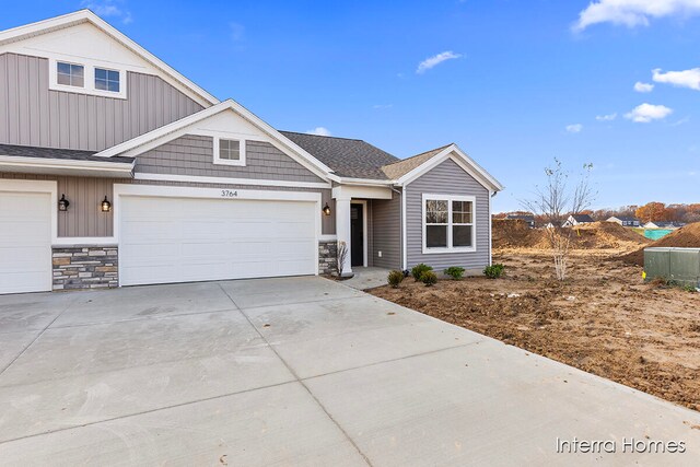 view of front of property with stone siding, an attached garage, concrete driveway, and a shingled roof