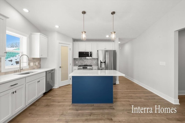 kitchen with baseboards, a kitchen island, a sink, appliances with stainless steel finishes, and white cabinetry