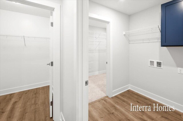 clothes washing area with hookup for a washing machine, cabinet space, wood finished floors, and baseboards