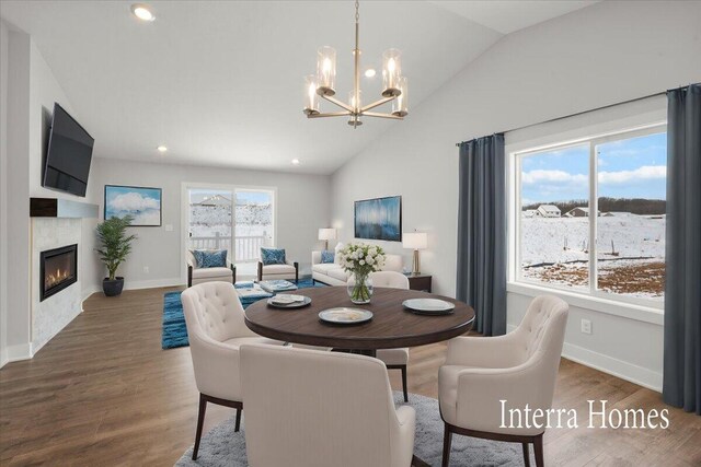 dining room featuring a glass covered fireplace, an inviting chandelier, wood finished floors, and vaulted ceiling