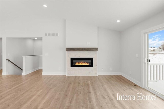 unfurnished living room with visible vents, light wood-style flooring, a glass covered fireplace, recessed lighting, and baseboards