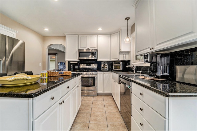 kitchen with white cabinetry, appliances with stainless steel finishes, dark stone countertops, backsplash, and pendant lighting