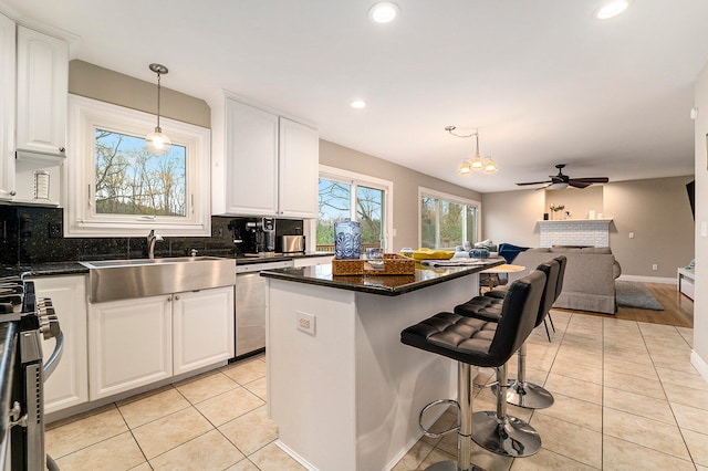 kitchen with a brick fireplace, stainless steel appliances, a center island, sink, and white cabinetry