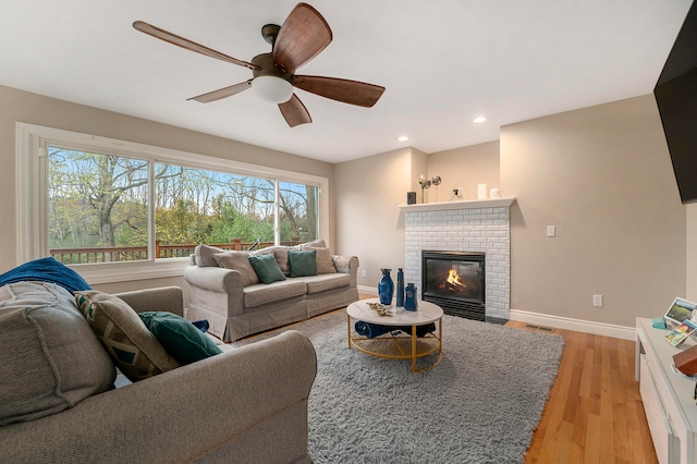 living room featuring a brick fireplace, light wood-type flooring, and ceiling fan