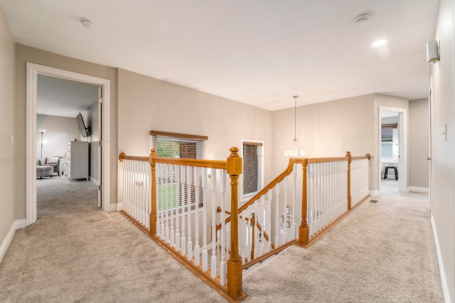 corridor featuring light colored carpet and a notable chandelier