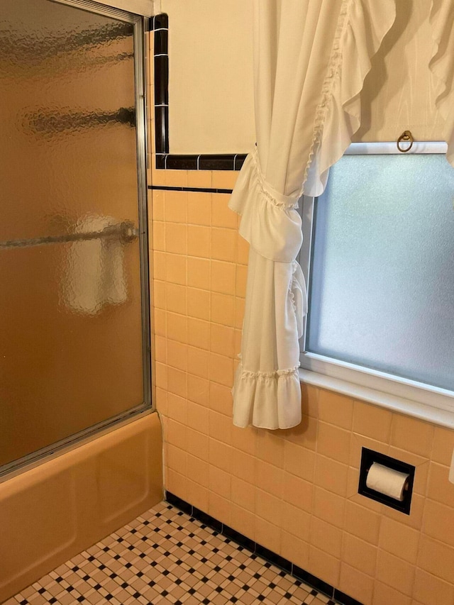 bathroom with tile walls, enclosed tub / shower combo, and tile patterned floors