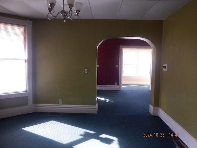 carpeted empty room featuring a notable chandelier and a wealth of natural light