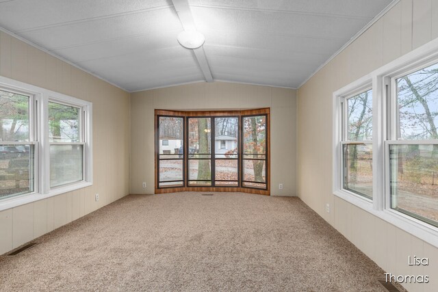 carpeted spare room featuring lofted ceiling with beams, a wealth of natural light, and crown molding