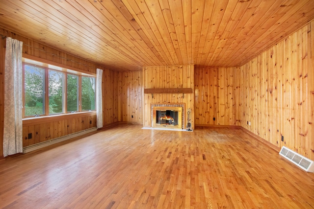 unfurnished living room featuring light wood-type flooring, wood walls, a tiled fireplace, wood ceiling, and baseboard heating