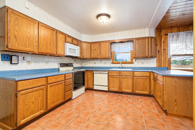 kitchen with wooden walls, sink, light tile patterned floors, backsplash, and white appliances