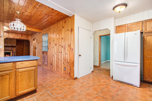 kitchen featuring light tile patterned flooring, white fridge, a fireplace, wood walls, and pendant lighting