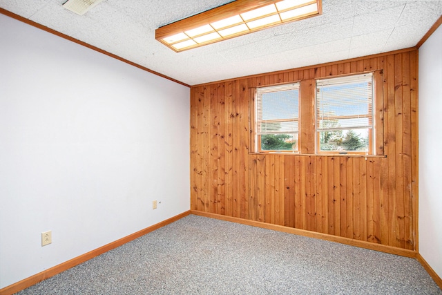 spare room with wood walls, a textured ceiling, crown molding, and carpet floors