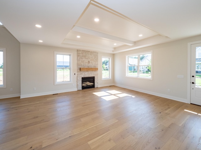 unfurnished living room featuring a stone fireplace, light wood-type flooring, and a tray ceiling