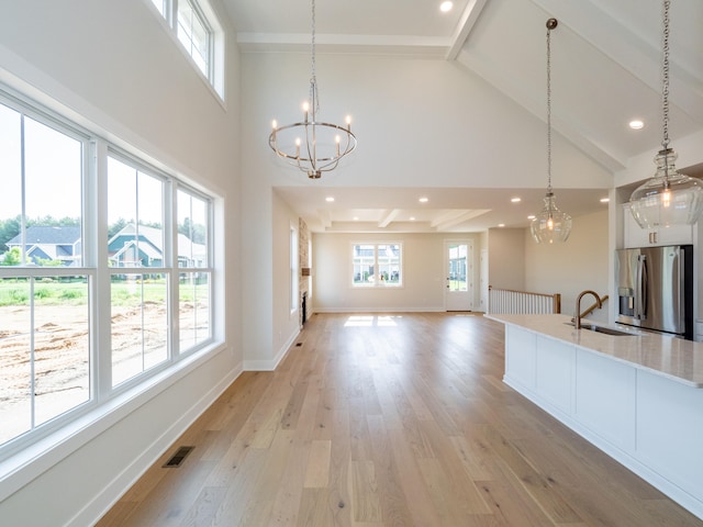 kitchen featuring light wood-type flooring, decorative light fixtures, high vaulted ceiling, stainless steel refrigerator with ice dispenser, and sink