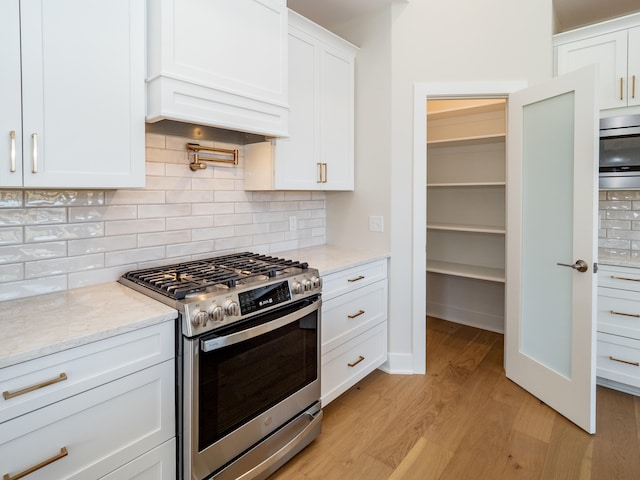 kitchen featuring light hardwood / wood-style floors, light stone counters, stainless steel range with gas cooktop, backsplash, and white cabinetry