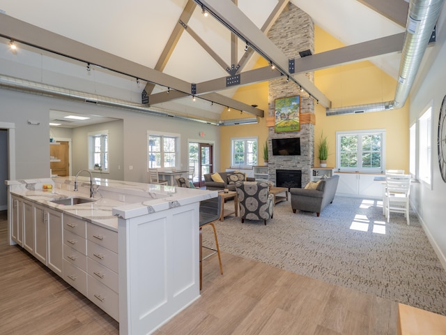 kitchen with a stone fireplace, white cabinetry, sink, and high vaulted ceiling