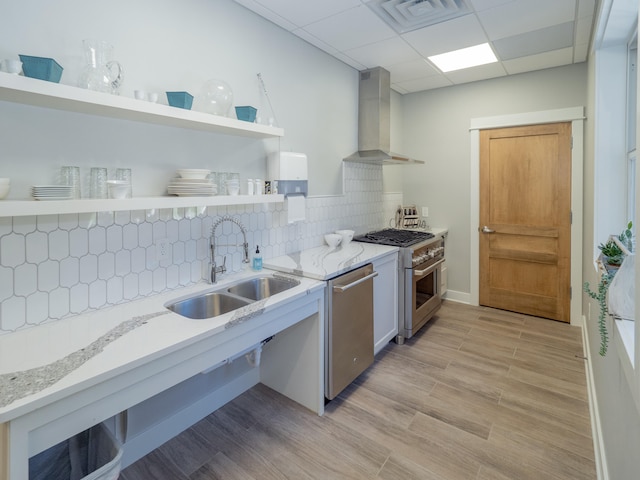 kitchen featuring light stone countertops, wall chimney range hood, sink, and appliances with stainless steel finishes