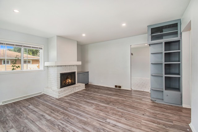 unfurnished living room featuring wood-type flooring, a brick fireplace, and a baseboard heating unit