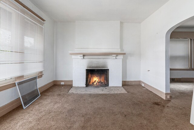 unfurnished living room featuring a brick fireplace and carpet floors