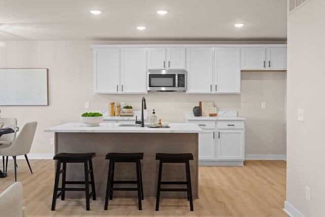 kitchen featuring white cabinetry, light hardwood / wood-style floors, an island with sink, and a kitchen bar