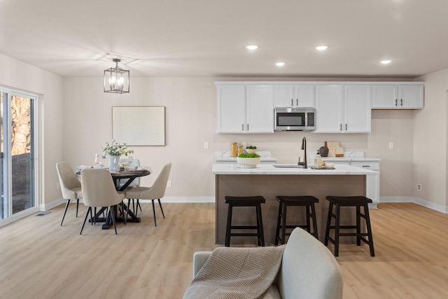 kitchen with sink, light wood-type flooring, a center island with sink, and white cabinets