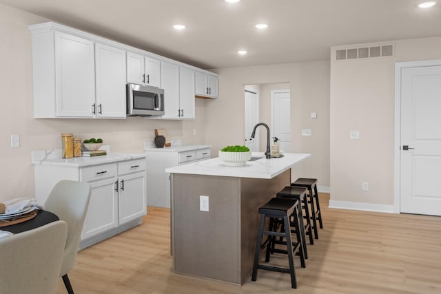 kitchen featuring an island with sink, white cabinets, a kitchen bar, light hardwood / wood-style floors, and light stone countertops