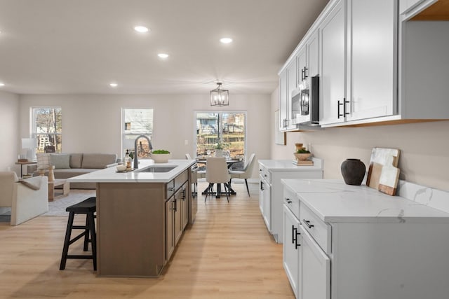 kitchen with sink, appliances with stainless steel finishes, white cabinets, a center island with sink, and light wood-type flooring