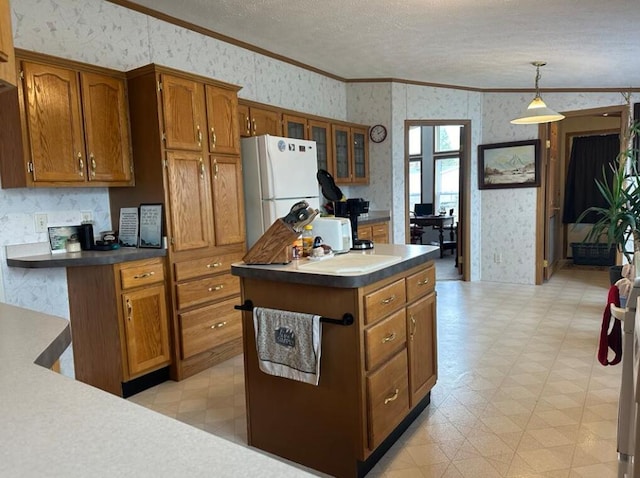 kitchen featuring ornamental molding, a kitchen island, white refrigerator, a textured ceiling, and hanging light fixtures