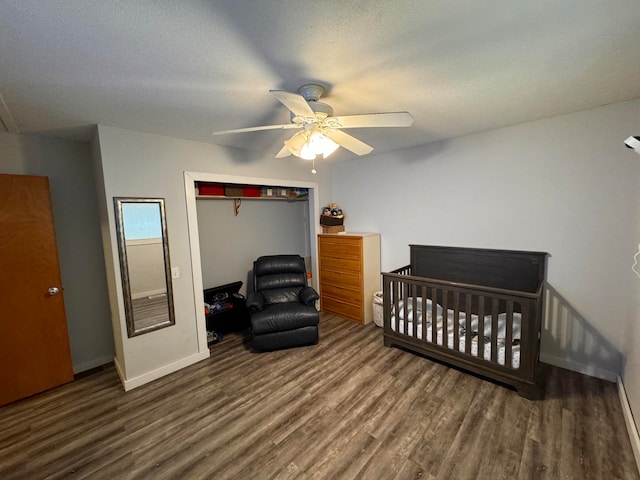 bedroom featuring a closet, a nursery area, a textured ceiling, dark wood-type flooring, and ceiling fan