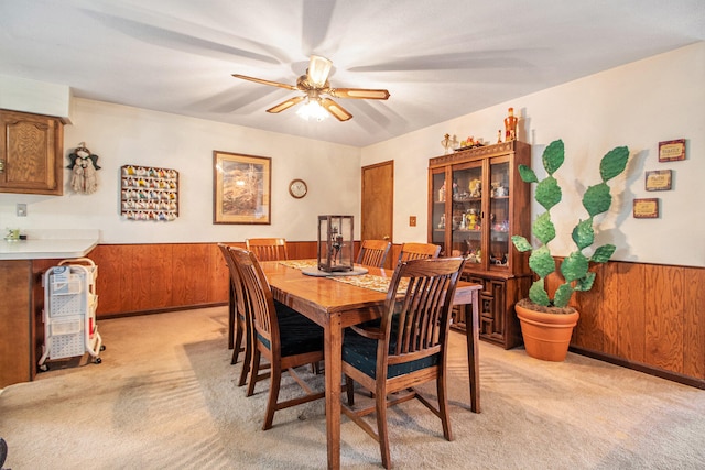 dining space featuring wooden walls, light colored carpet, and ceiling fan