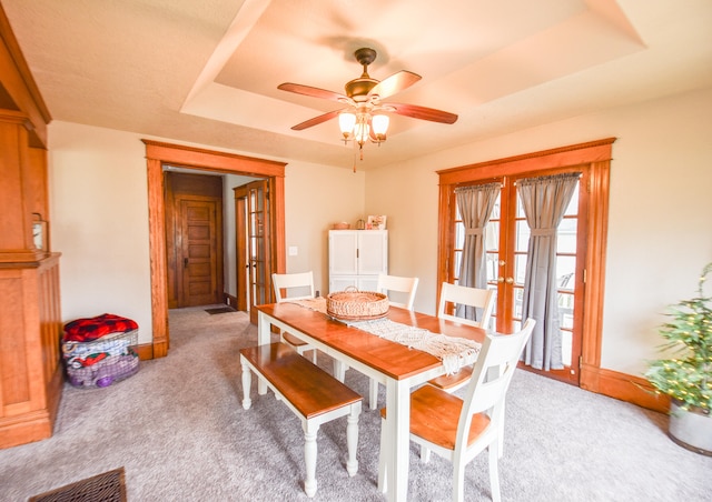 dining space featuring a raised ceiling, ceiling fan, french doors, and light carpet