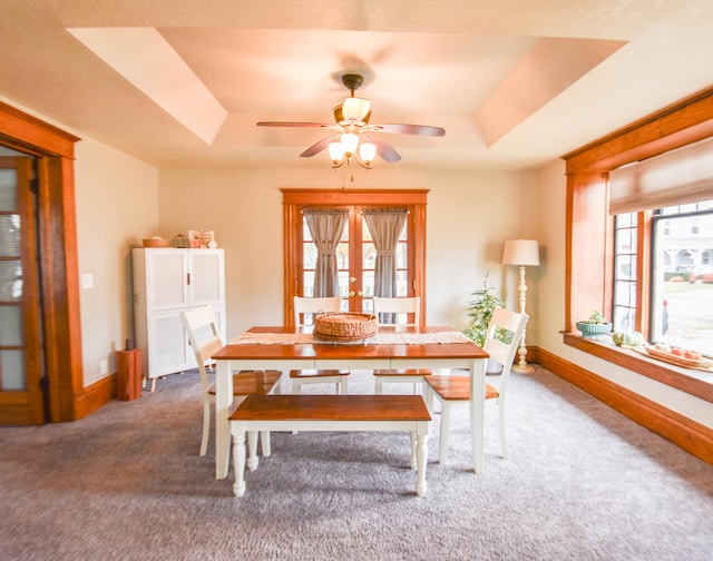 carpeted dining room featuring ceiling fan and a raised ceiling