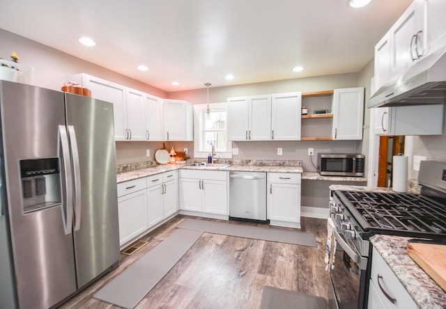 kitchen with appliances with stainless steel finishes, sink, exhaust hood, pendant lighting, and white cabinets