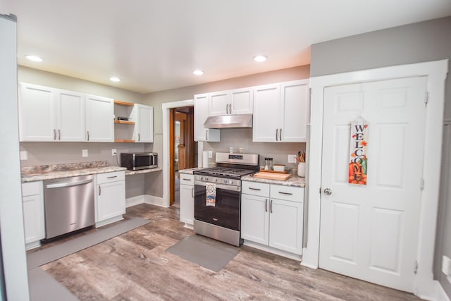 kitchen with appliances with stainless steel finishes, light hardwood / wood-style floors, white cabinetry, and light stone counters